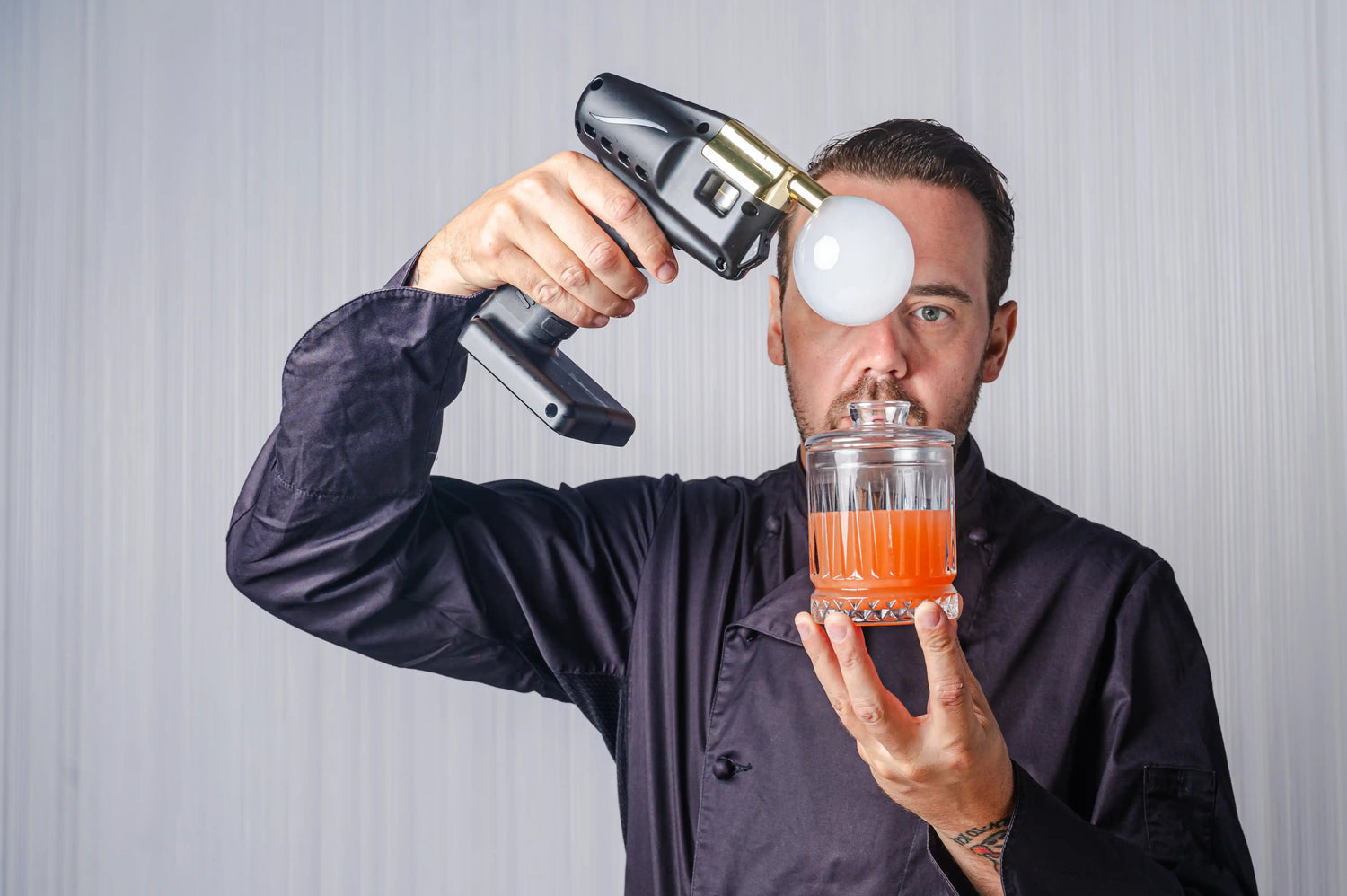 simone caporale holding aroma gun with bubble to face holding a rocks glass